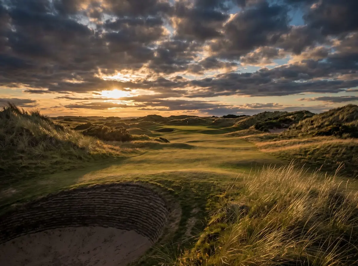 Championship links golf course with dunes and pot bunkers at golden hour.