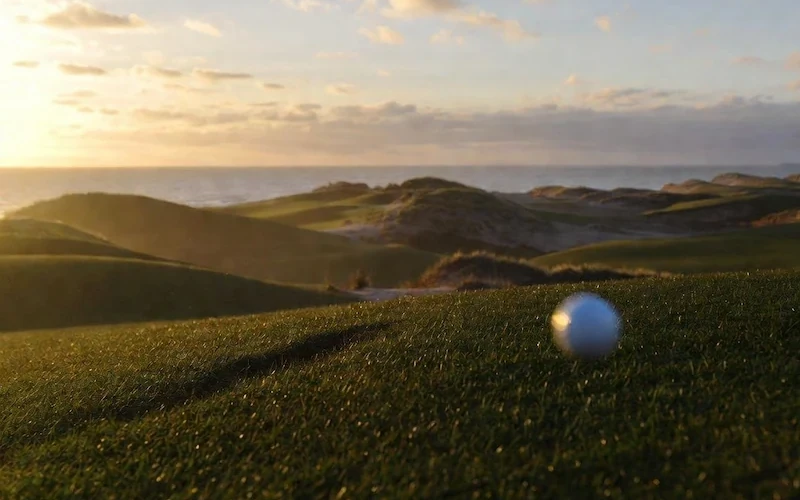 Rolling links fairway running between grass-covered dunes near the sea.
