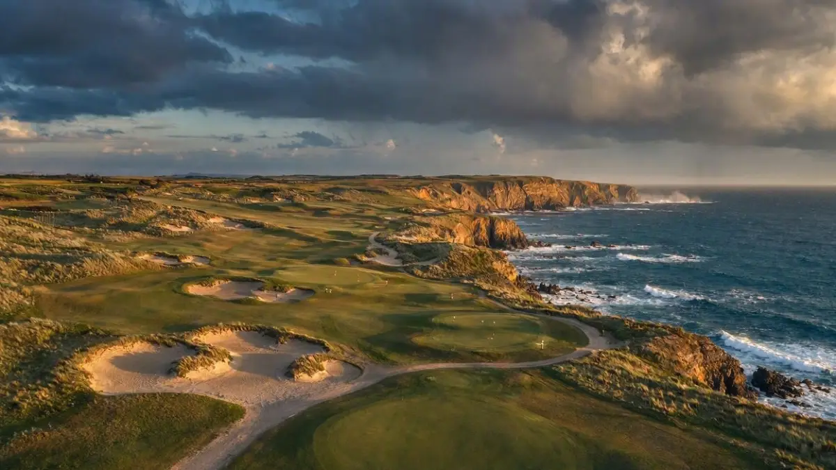 Aerial view of a links golf course along a rugged coastline at golden hour